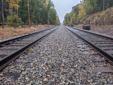 This is a long-angle picture of a set of train tracks separated by rocks and surrounded by green trees.
