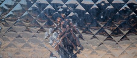 What appears to be a woman taking a photo in a shiny, reflective geometric pattern so that we only see her reflection.